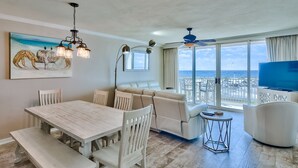 En rummelig opholdsstue med spisebord, sofa og fjernsyn, der giver udsigt til en balkon med havudsigt.