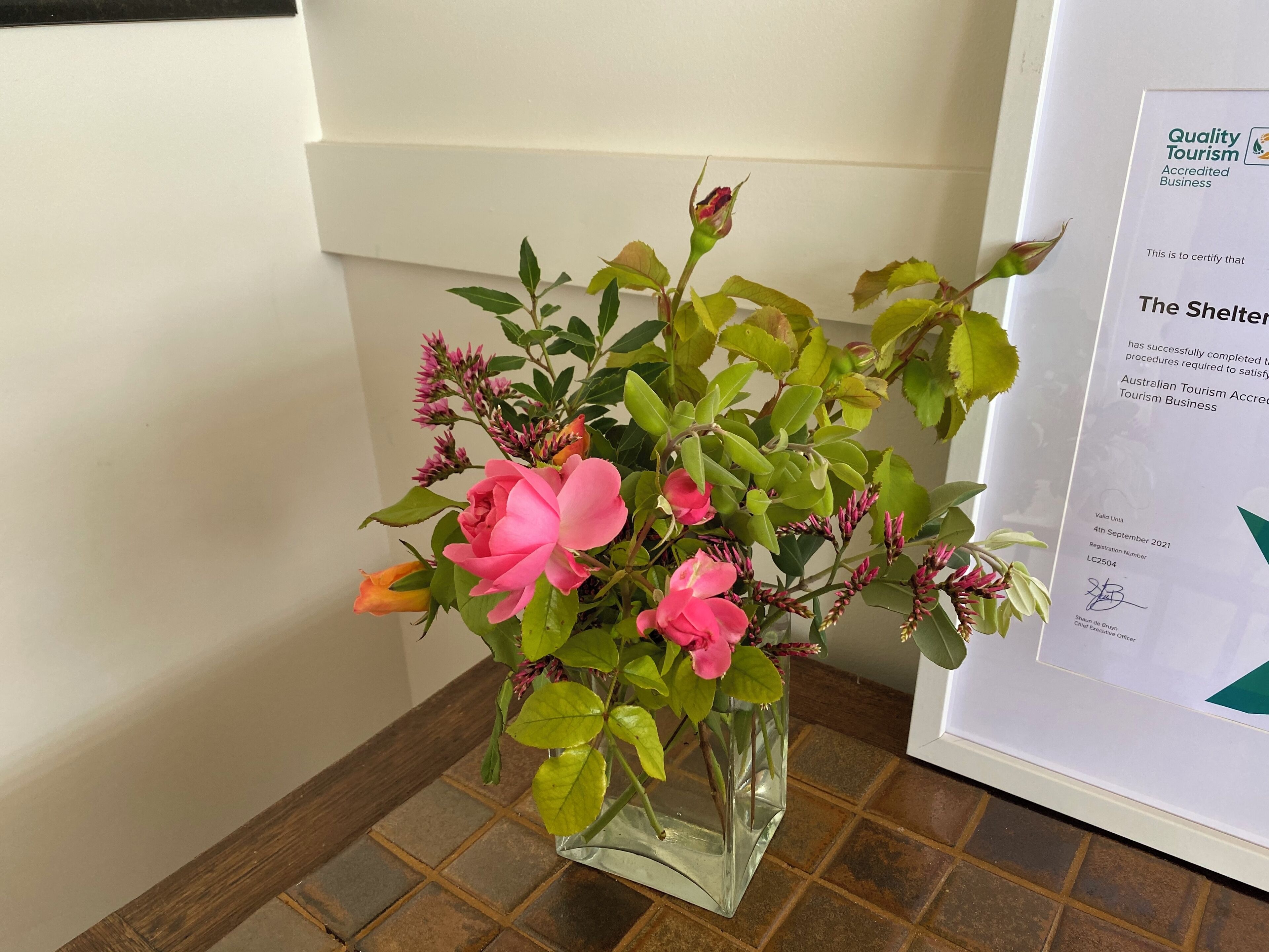 A clear glass vase with pink flowers and green leaves on a tiled floor.