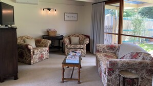 A cozy living room with floral-patterned sofas, a wooden coffee table, a television on a cabinet, and a window with curtains. - The Shelter bnb @ Robe SA (Robe)