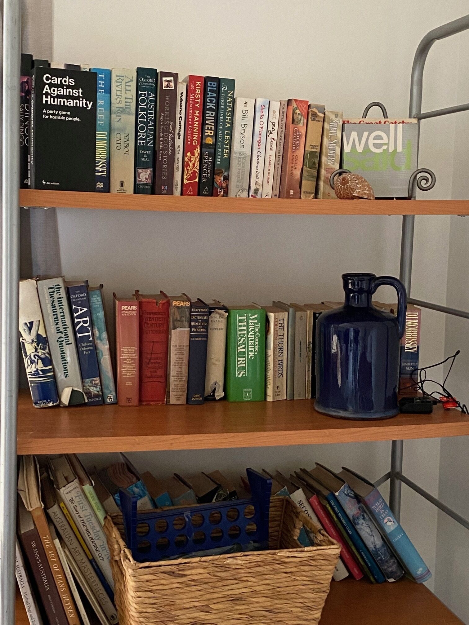 Ein Bücherregal mit verschiedenen Büchern, einer blauen Tasse und einem Korb voller Zeitschriften.