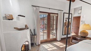 Una habitación con chimenea, suelo de madera, cama, lámpara y vistas a través de un ventanal.