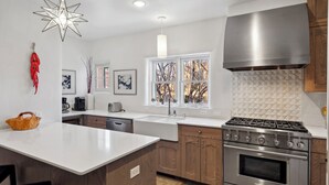 Una cocina moderna con una isla central, electrodomésticos de acero inoxidable, armarios de madera y un amplio ventanal con vistas a árboles.