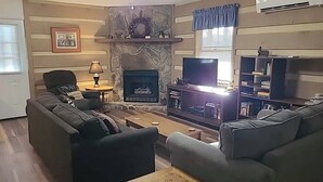 Una sala de estar con chimenea de piedra, televisor y estantería.