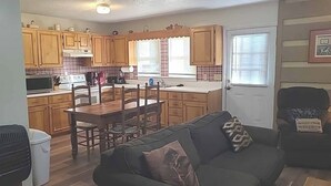 Una cocina con armarios de madera, una mesa de comedor y sillas. Hay un sofá con un cojín en la zona de estar.