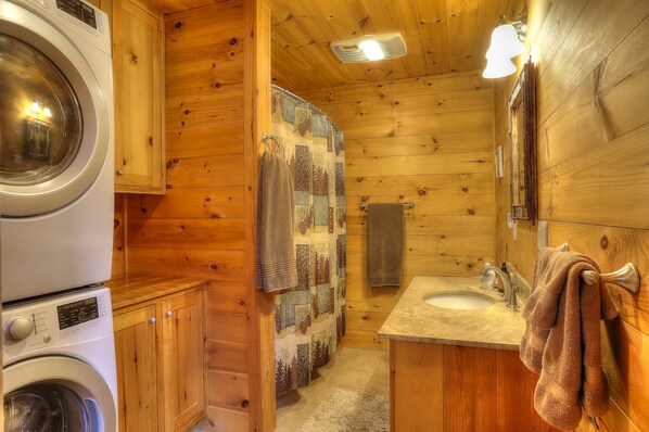 A wooden cabin bathroom with a washing machine, a shower curtain, a sink, and a towel rack. - 7 Terraces Way - Beautiful, brand new home near the Terraces cottage community (Rangeley)