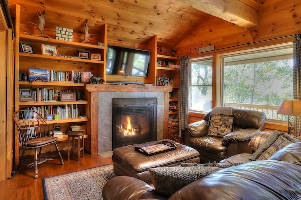 A cozy living room with a fireplace, leather furniture, and a bookshelf filled with books. - 7 Terraces Way - Beautiful, brand new home near the Terraces cottage community (Rangeley)