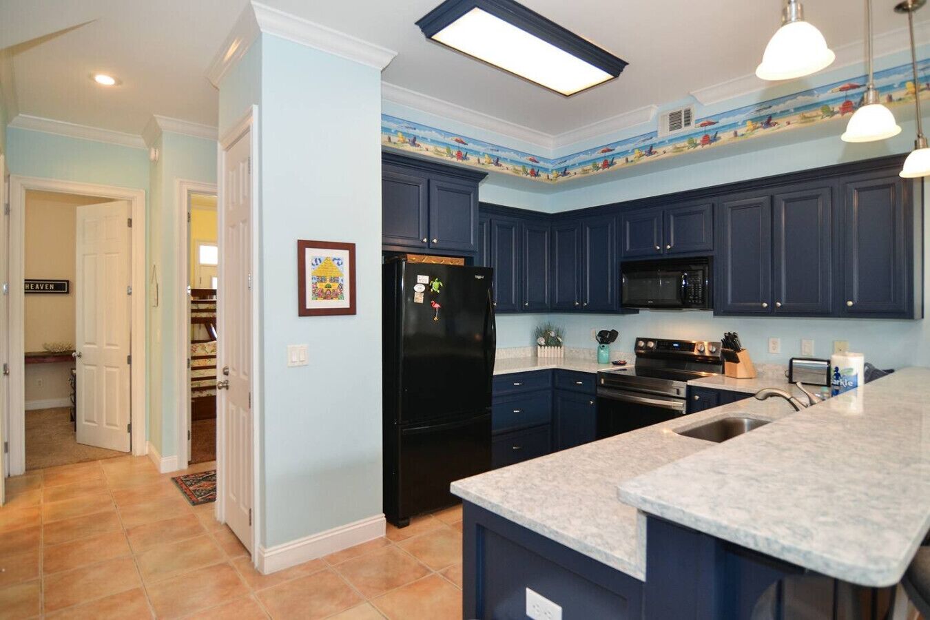 A modern kitchen with dark blue cabinets, a black refrigerator, a microwave, and a granite countertop.