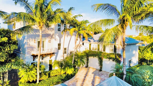 A white building with multiple balconies, surrounded by palm trees and lush greenery. - Luxury Beach Retreat - 200 Steps to Beach - Heated Pool, Spa & Elevator (Jupiter)