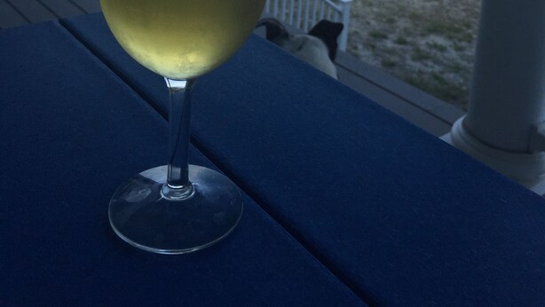 Ett glas vitt vin på ett blått bord på en veranda med utsikt över en strand.