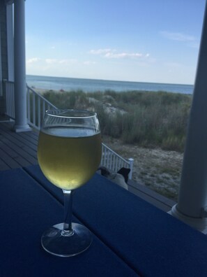 A glass of white wine on a blue table on a porch overlooking a beach.