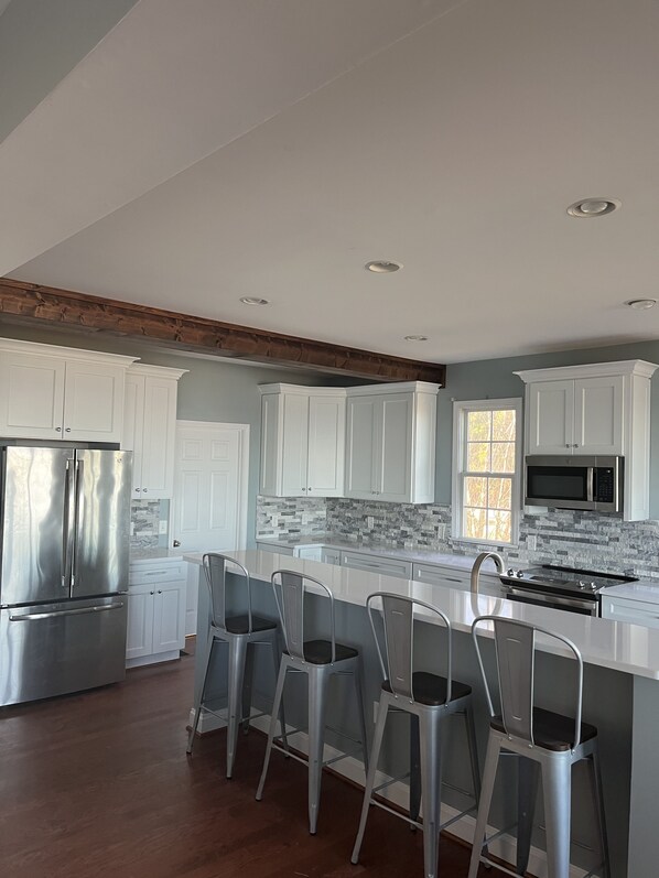 A modern kitchen with white cabinetry, a stainless steel refrigerator, a built-in microwave, and a large island with bar stools.