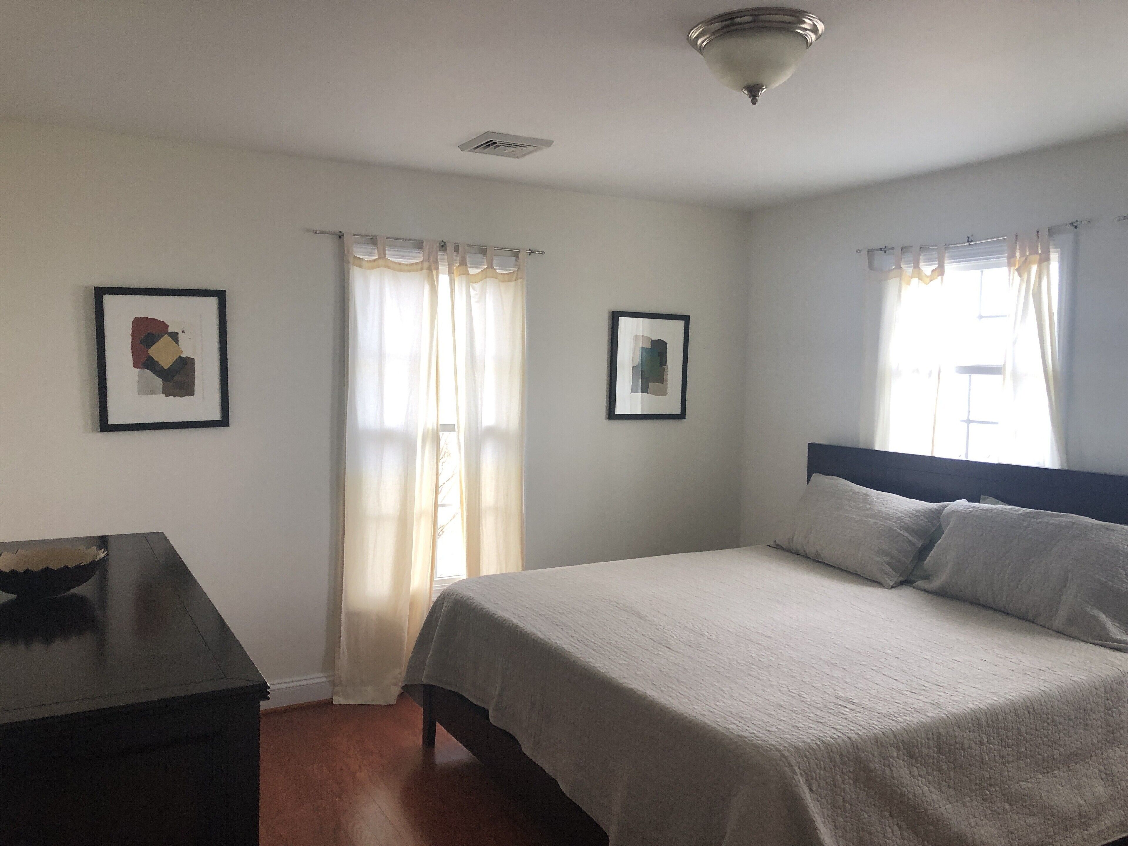 A bedroom with a bed, two framed pictures, a desk, and a window with curtains.