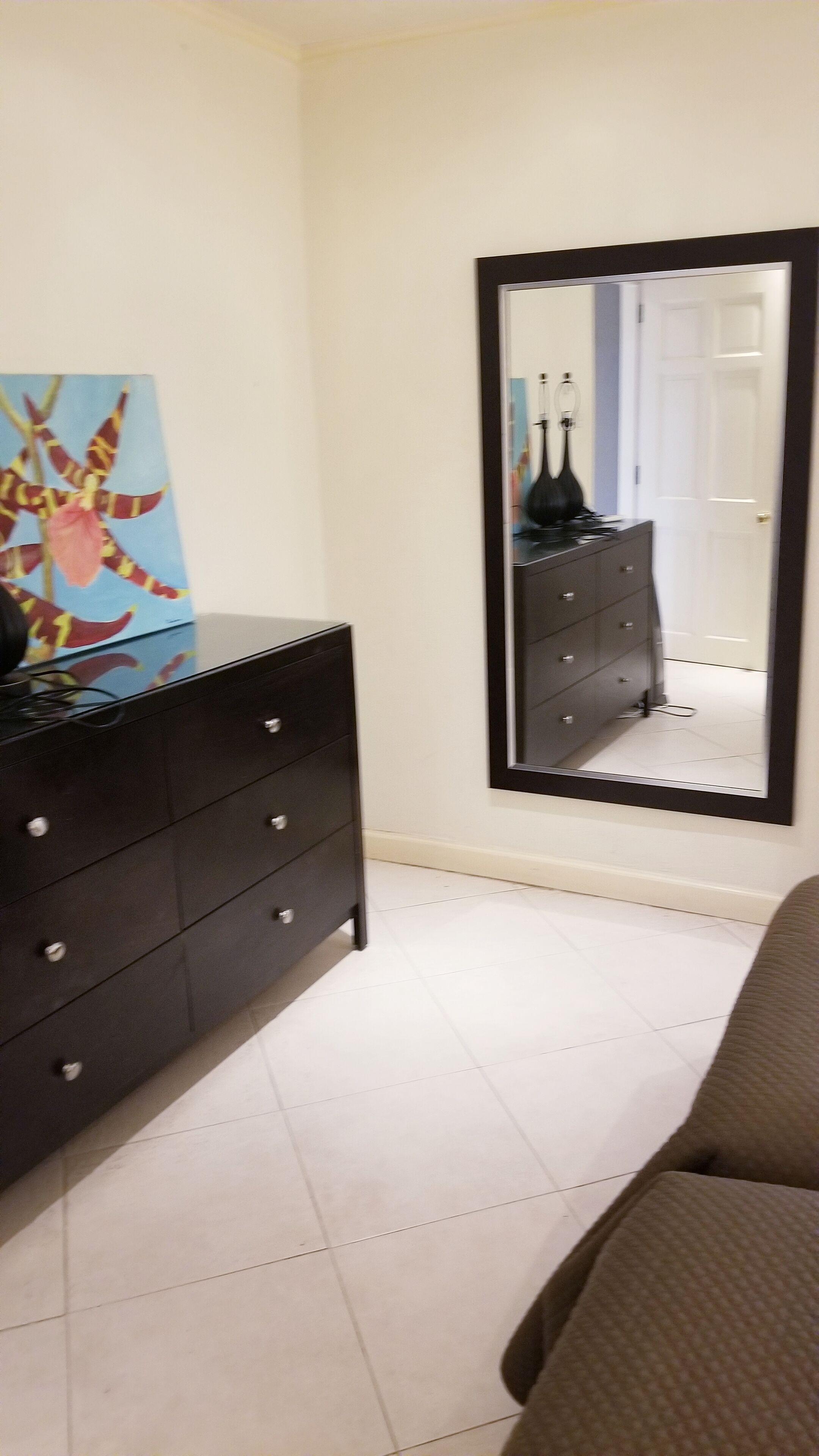 Un dormitorio con un aparador negro, un espejo grande y un cuadro en la pared.