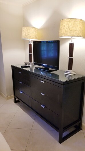 A dark wooden TV stand with a flat-screen TV, two lamps, and three drawers. - Modern Barbados condo with WIFI,  walk out to POOL, steps from BEACH (Hastings)