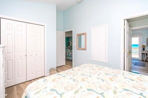 Un dormitorio con cama, armario, espejo y vistas a la playa a través de una puerta abierta.