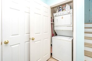 A laundry room with a washing machine and dryer, a door with a brass handle, and a red mop leaning against the wall. - Sundog - Spacious 4 BR Oceanfront Home with 2 Sun Decks (North Topsail Beach)