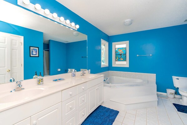 A bathroom with a white vanity, a large mirror with lights, a bathtub, and a toilet.