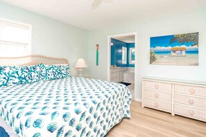 A bedroom with a bed, a nightstand, a dresser, a bathroom with a bathtub, and a painting of a beach scene. - Sundog - Spacious 4 BR Oceanfront Home with 2 Sun Decks (North Topsail Beach)