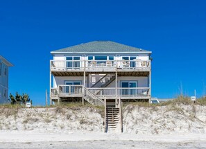 A two-story beachfront house with a wooden deck and a staircase leading to the upper floor.