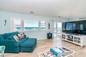 A living room with a teal sofa, a coffee table with magazines, a TV, and a bookshelf. - Sundog - Spacious 4 BR Oceanfront Home with 2 Sun Decks (North Topsail Beach)