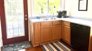 A compact kitchen with wooden cabinets, a Bosch dishwasher, and a window with a view of greenery. - Quiet oasis across the street from Acadia and just steps from the harbor (Seal Harbor)