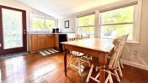 A spacious kitchen with wooden cabinets, a dining table, and chairs. There are large windows providing natural light. - Quiet oasis across the street from Acadia and just steps from the harbor (Seal Harbor)