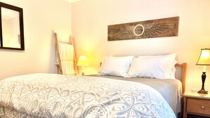 A neatly made bed with patterned bedding, a wooden headboard, a wall-mounted artwork, a bedside lamp, and a nightstand with a lamp. - Quiet oasis across the street from Acadia and just steps from the harbor (Seal Harbor)