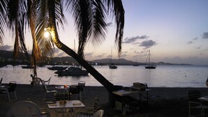 Ein Restaurant am Strand mit Außenbereich, das auf ruhiges Wasser und Boote mit Blick auf eine Palme blickt.