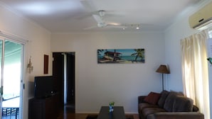 A living room with a ceiling fan, a painting of a beach scene, a sofa, a coffee table, and a TV.