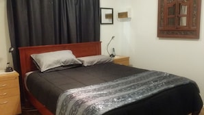 A single bed with a wooden headboard, a bedside table with a lamp, and a nightstand with a phone.