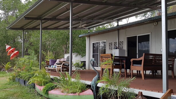 A covered outdoor seating area with wooden chairs and tables, surrounded by potted plants and a decorative bird sculpture.