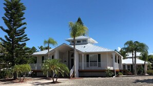 A two-story house with a porch, surrounded by trees and a gravel driveway. - Key West Style Florida Charm w Heated Private Salt Pool, close walk to Beach (Marco Island)