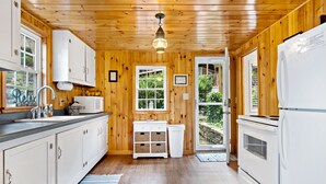 Une cuisine avec des murs en bois, des armoires blanches, un évier, un four à micro-ondes et un réfrigérateur.