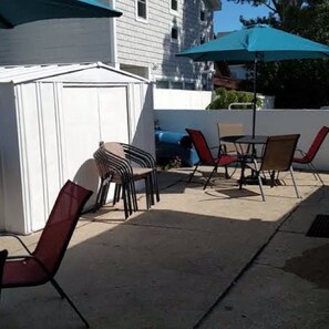 Un patio al aire libre con un cobertizo blanco, una mesa con sillas y una sombrilla azul.