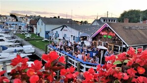 Een bar aan het water met terras, boten afgemeerd in de buurt, en een gebouw met de tekst 'Captain Louie's Bar Grill'.