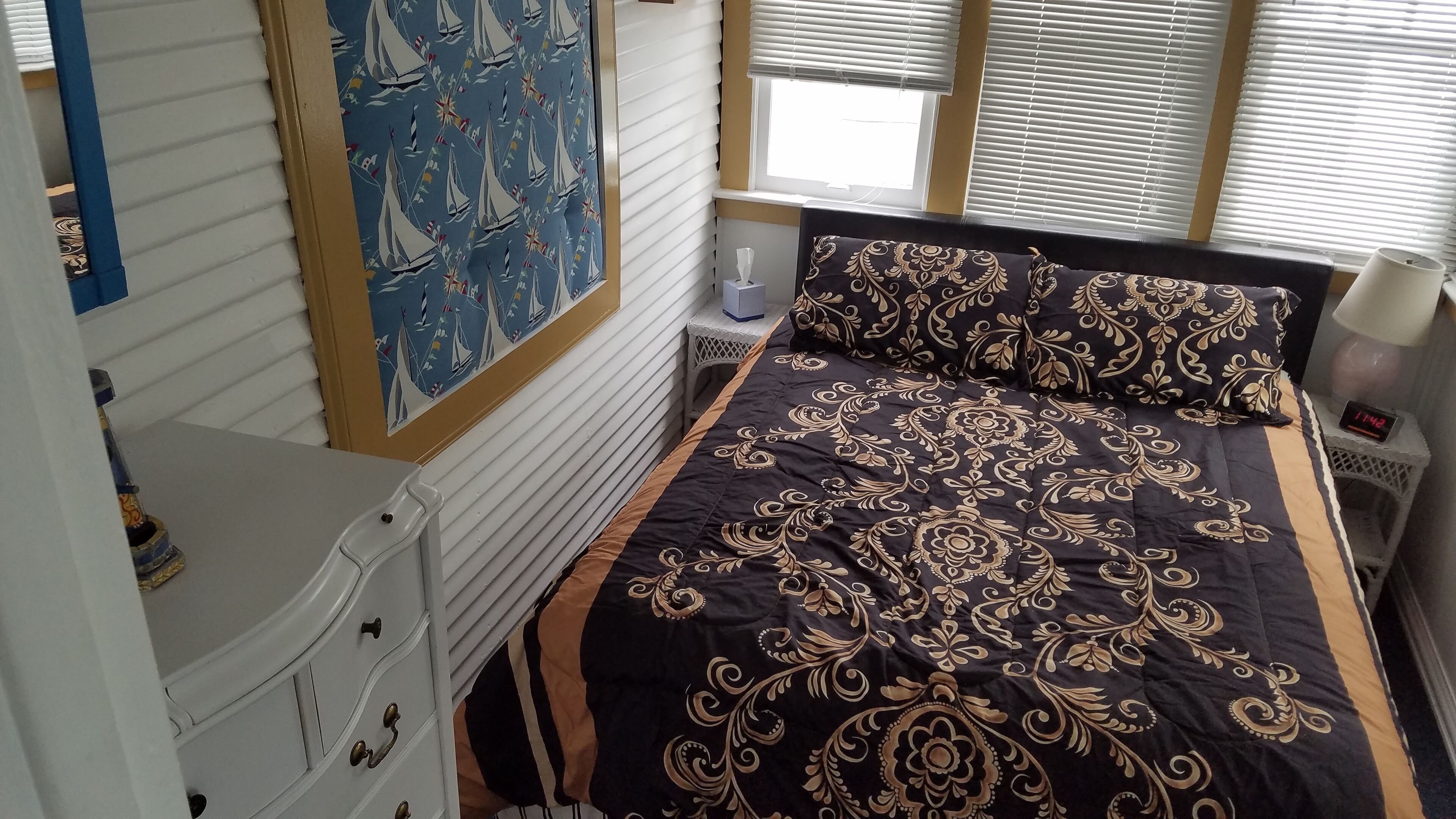 Un dormitorio con una cama, una mesita de noche, una lámpara, un reloj de pared y una ventana con persianas.