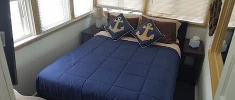 A neatly made bed with a blue bedspread and two pillows with anchor designs.