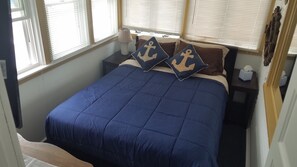 Una cama bien hecha con una colcha azul y dos almohadas con motivos de anclas.