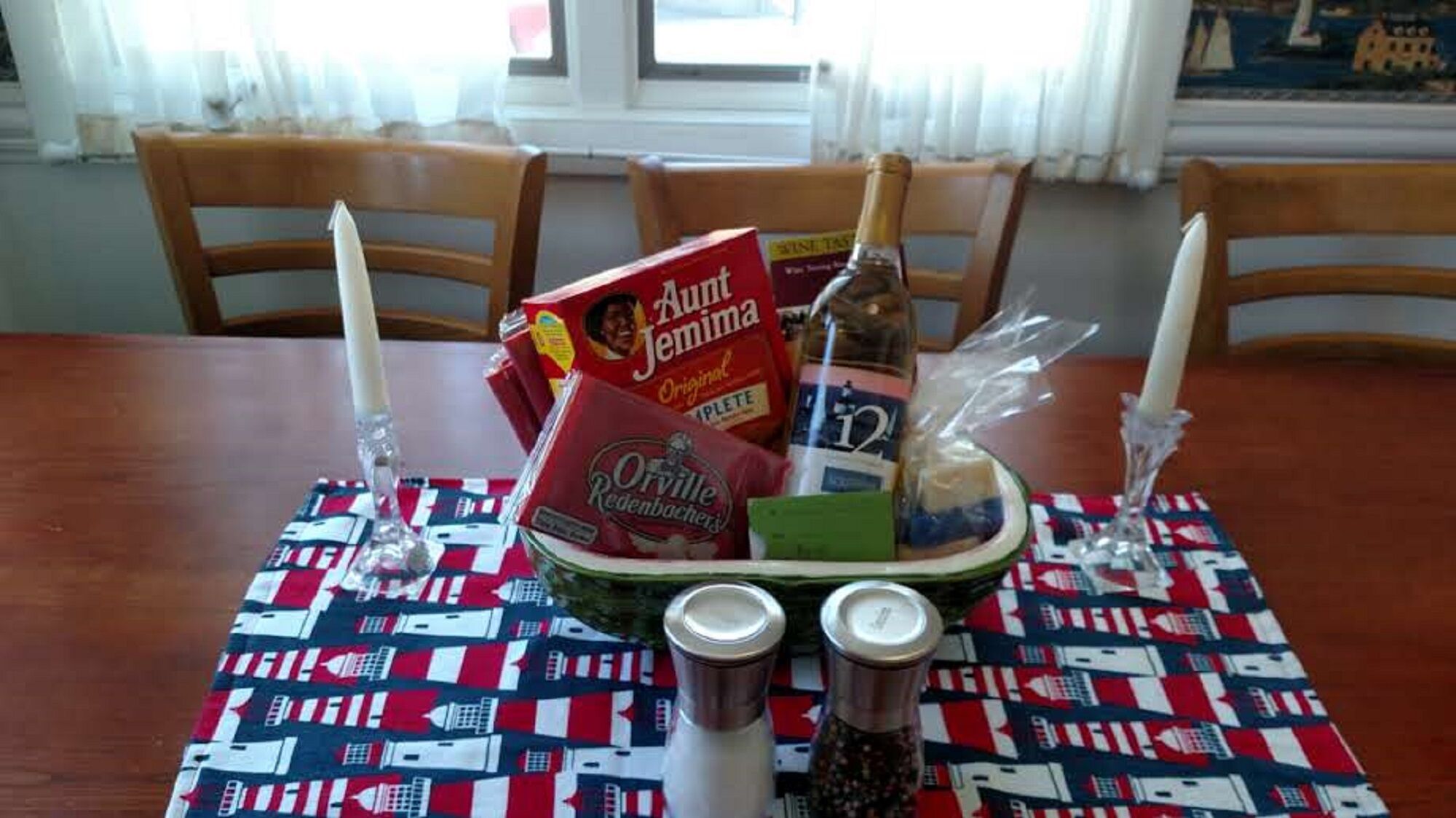 A dining table with a patriotic tablecloth, a bottle of wine, salt and pepper shakers, a box of Aunt Jemima pancake mix, and a bottle of Orville Redenbacher's popcorn.