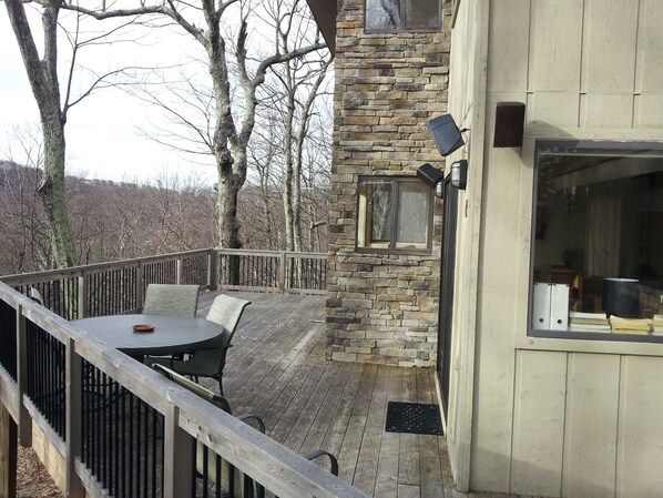 Una terraza con mobiliario exterior, un muro de piedra y una ventana con vista a árboles.