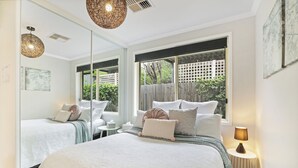 Quarto com cama grande, mesa de cabeceira, abajur e janela com vista para o exterior.