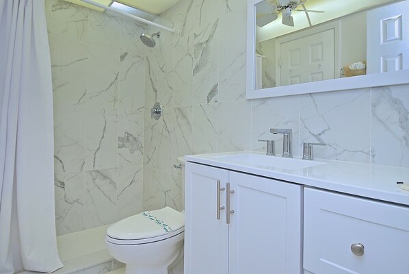 A bathroom with a shower, toilet, and vanity with a mirror.