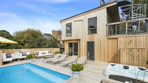 Ein moderner Poolbereich im Freien mit Holzterrasse, Liegestühlen und einem Whirlpool.