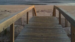 Ein hölzerner Steg führt zu einem Strand, der bei bewölktem Himmel und einem sichtbaren Mond liegt.