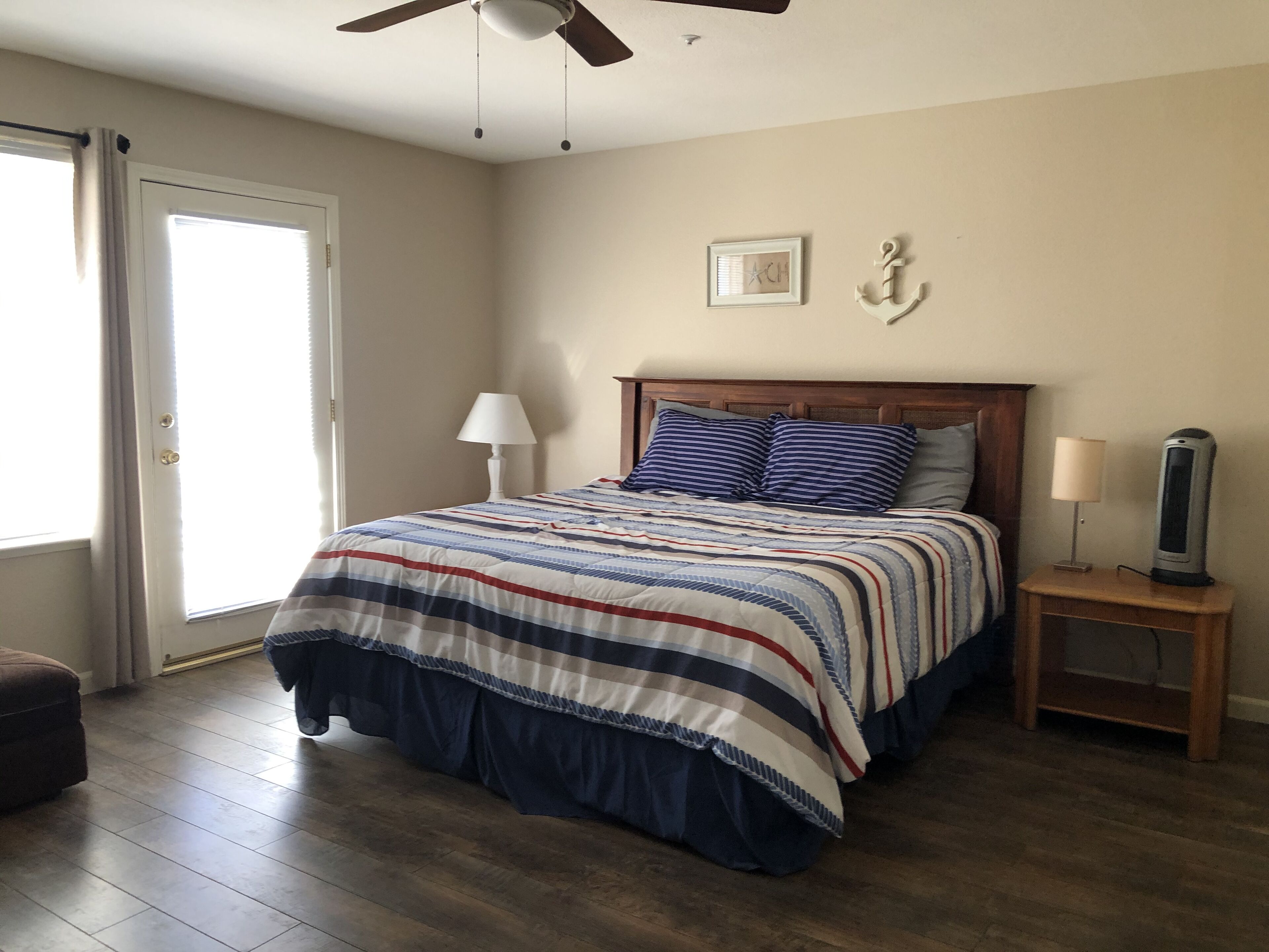 A bedroom with a bed, a nightstand, a ceiling fan, a door, and a window.