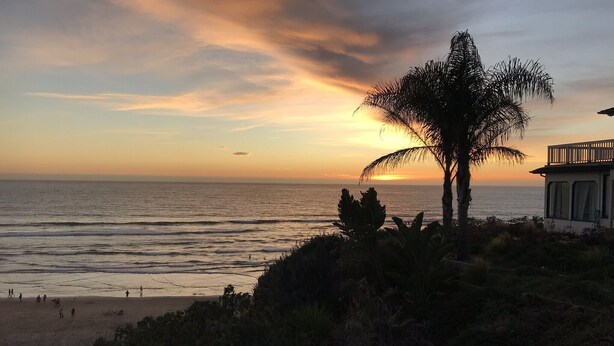 A beach with a wooden staircase leading down to the shore, a palm tree, and a building with a balcony overlooking the ocean. - Great location! Easy beach access! Sleeps 12 (Pismo Beach)