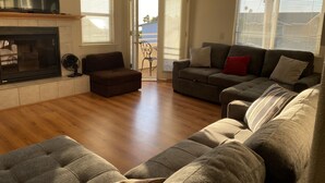 A living room with a fireplace, two sofas, a TV, and a sliding glass door leading to a balcony. - Great location! Easy beach access! Sleeps 12 (Pismo Beach)