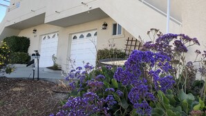 A two-story building with a white facade, multiple windows, and a visible garage door. - Great location! Easy beach access! Sleeps 12 (Pismo Beach)