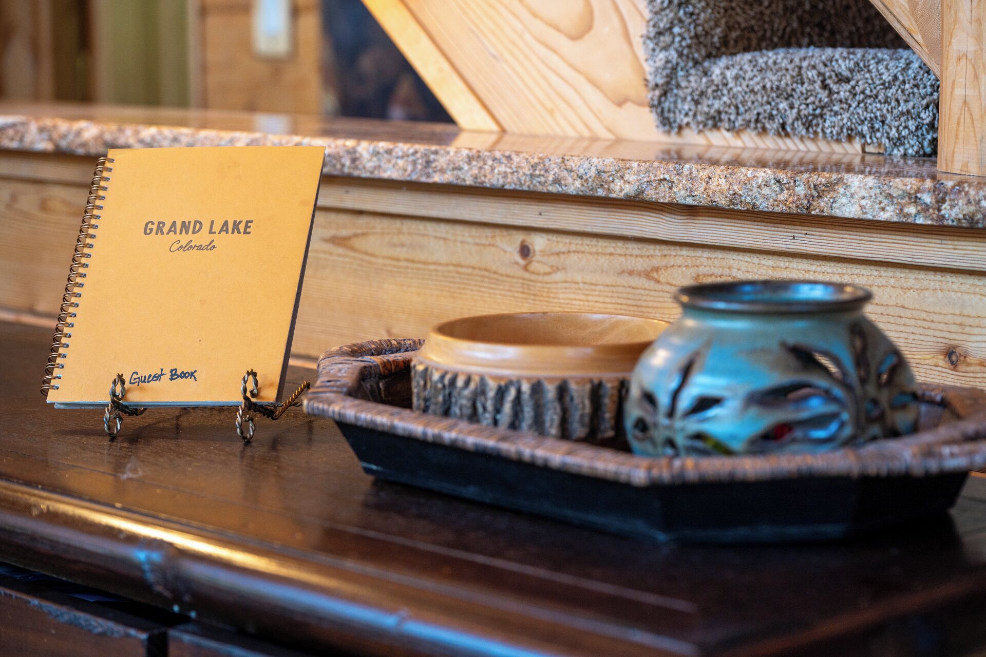 A notebook titled "Grand Lake Colorado" on a wooden surface with a ceramic bowl and a decorative vase.