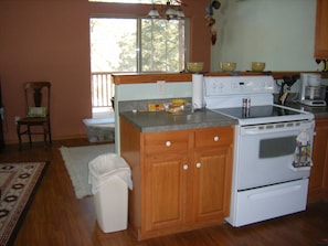 Une cuisine avec des meubles de rangement en bois, une cuisinière blanche et une fenêtre avec des stores.